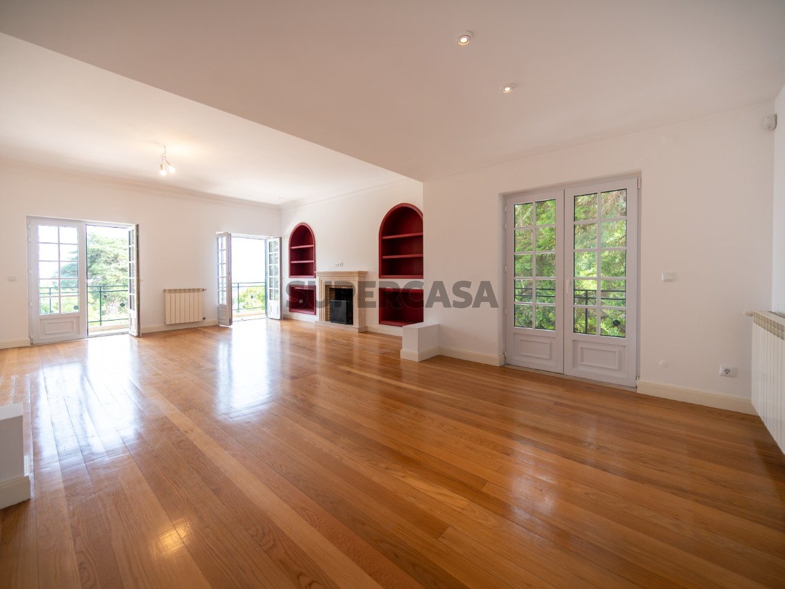 Sala espaçosa com lareira, pavimento em madeira e luz natural abundante, Moradia T4 + 1 | Cascais