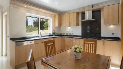 Cozinha equipada de penthouse à venda na Quinta da Boa Nova, Algarve. Armários em madeira, bancada preta e mesa de jantar.